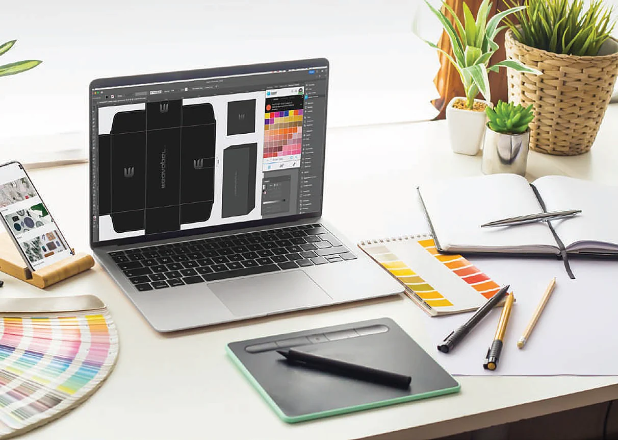 Designer’s desk with packaging dielines on a laptop and colour swatches